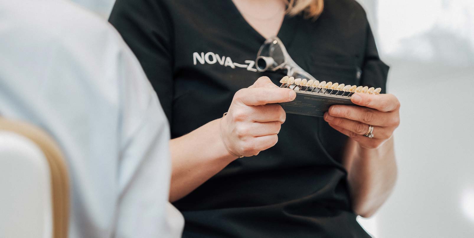 Detailbild einer Dentalhygienikerin von NOVA–Z, welche eine Zahnfarbskala in den Händen hält für ein Bleaching