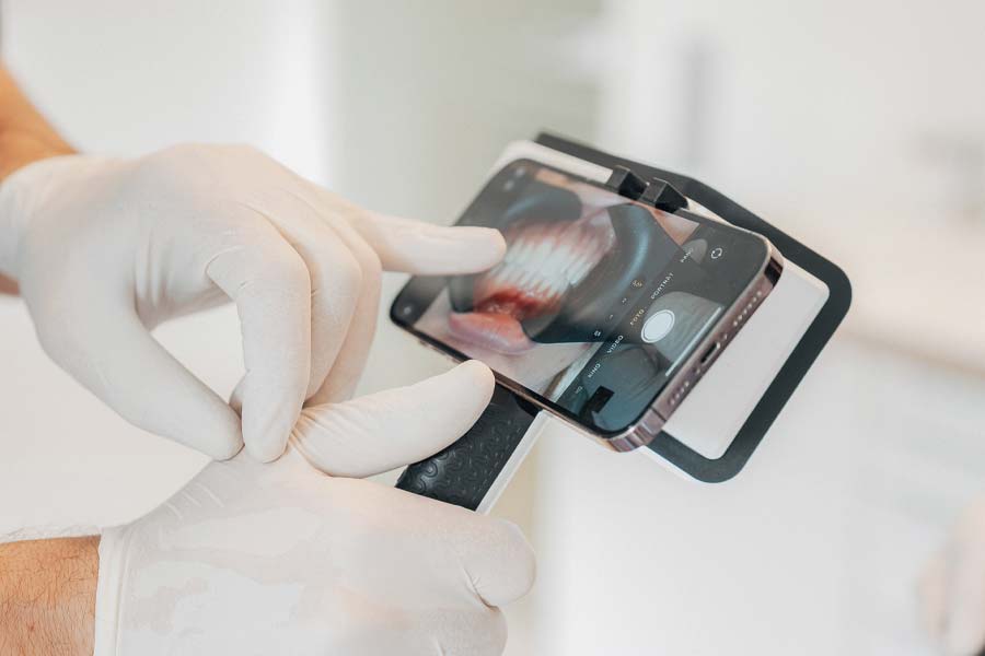Detailbild eines iPhones, auf dem ein Gebiss zu sehen ist. Hände in weißen Handschuhen halten das iPhone in einem Halter fest und zeigen auf das Gebiss
