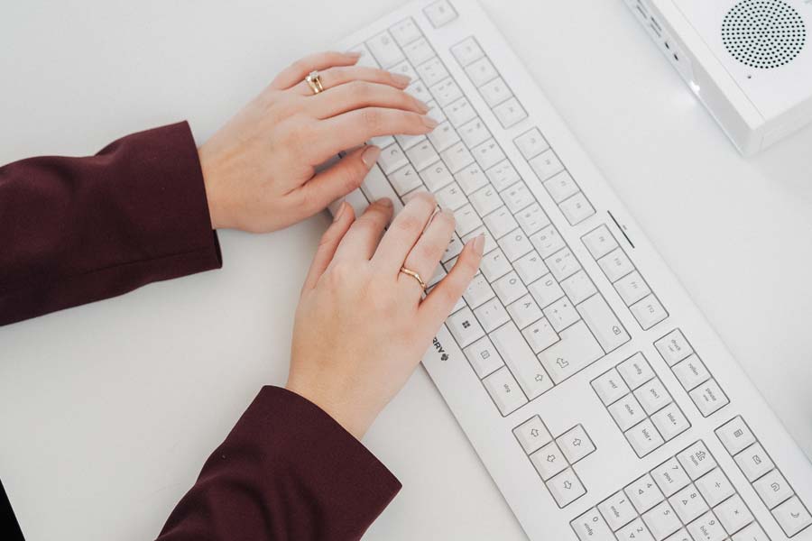 Hände einer Empfangsdame von NOVA–Z schreiben etwas auf einer hellen Computertastatur.