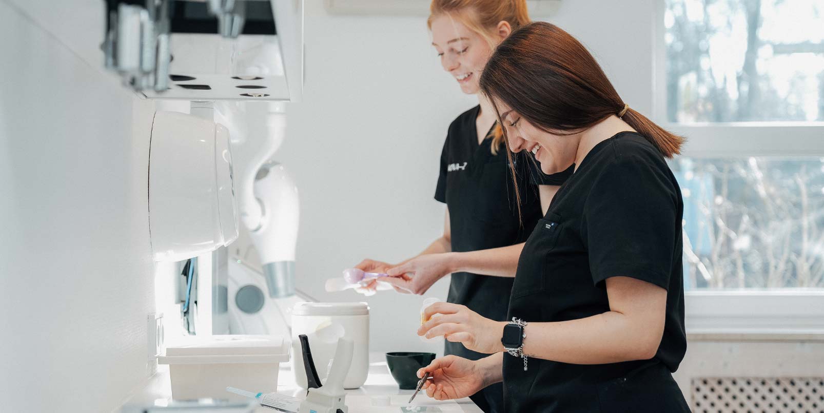 Zwei zahnmedizinische Fachangestellte bereiten einen Behandlungsplatz vor in der hellen und freundlichen Zahnarztpraxis NOVA–Z in München Harlaching