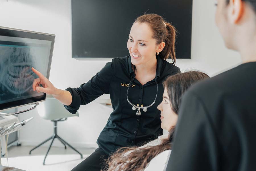Zahnärztin Nathalie Schubert von NOVA–Z erklärt einer Patientin etwas auf einem Bildschirm, der ein Röntgenbild ihres Gebisses zeigt. Die Zahnärztin lächelt dabei sympathisch.
