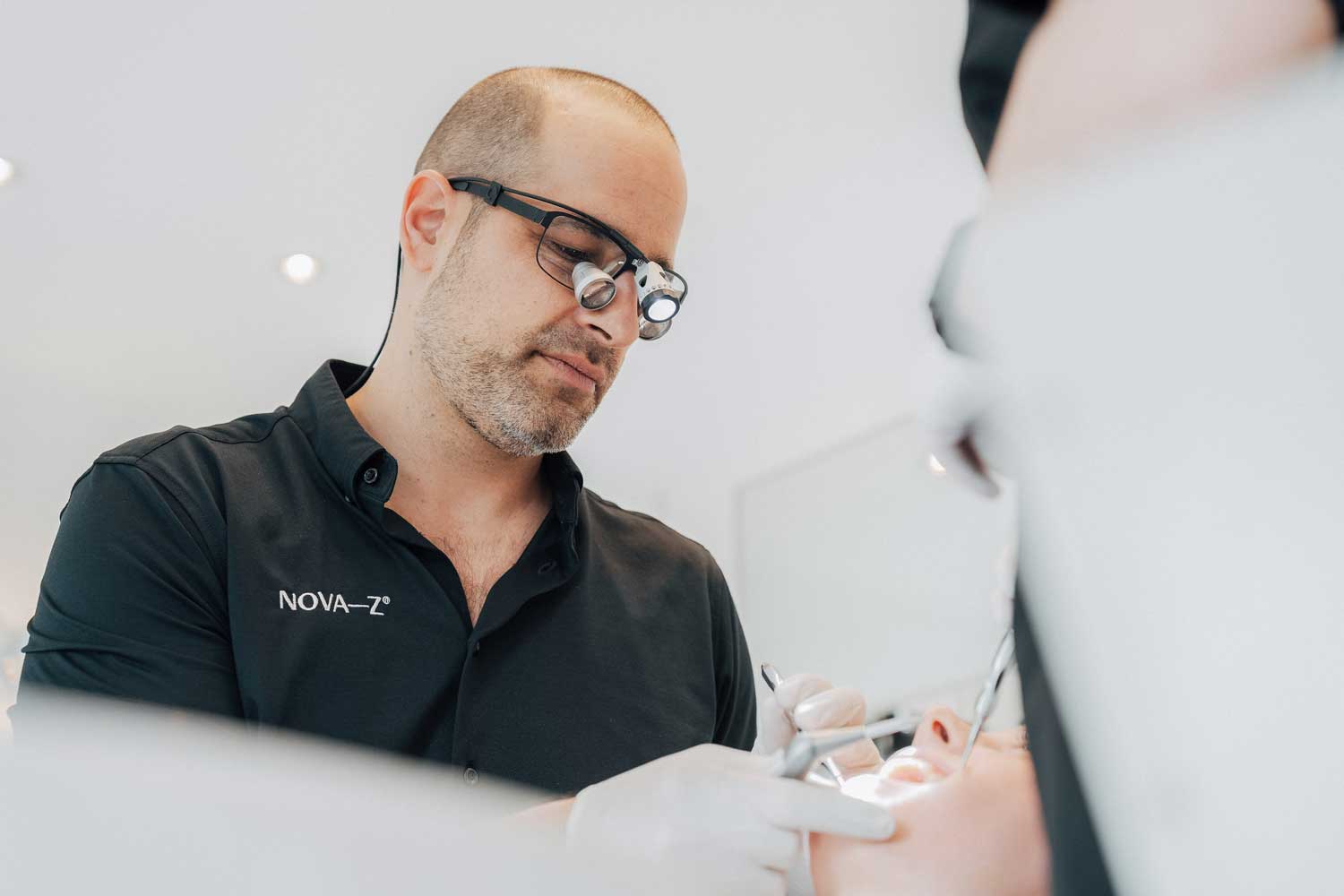 Dr. Denis Novakovic behandelt mit einer Lupenbrille eine Patientin
