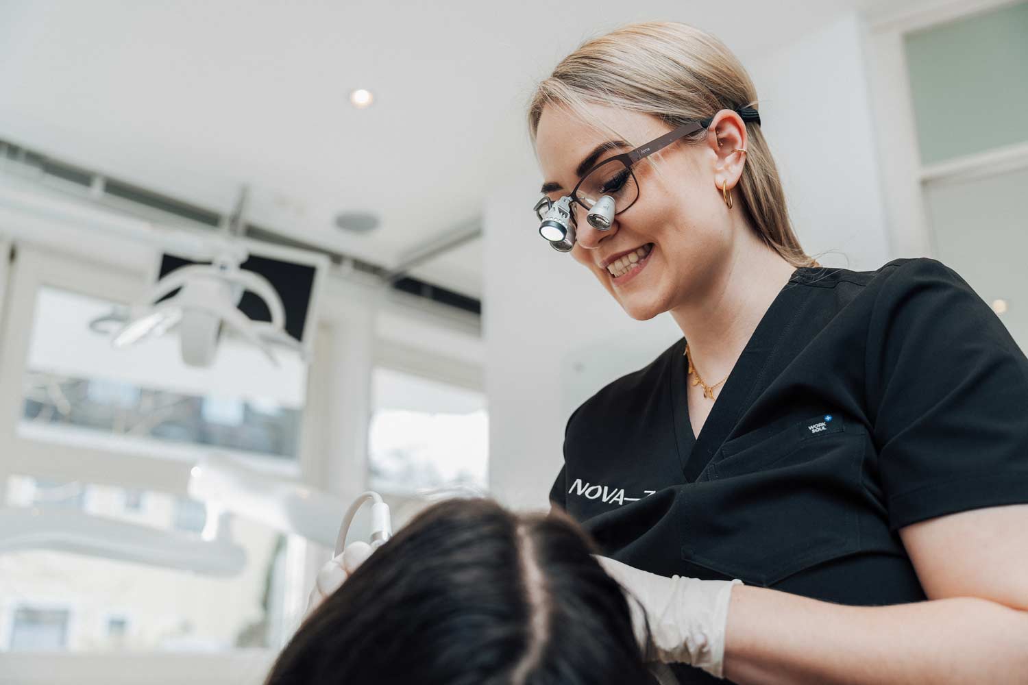 Eine Dentalhygienikerin von NOVA-Z trägt eine Lupenbrille und führt eine Professionelle Zahnreinigung bei einer Patientin durch