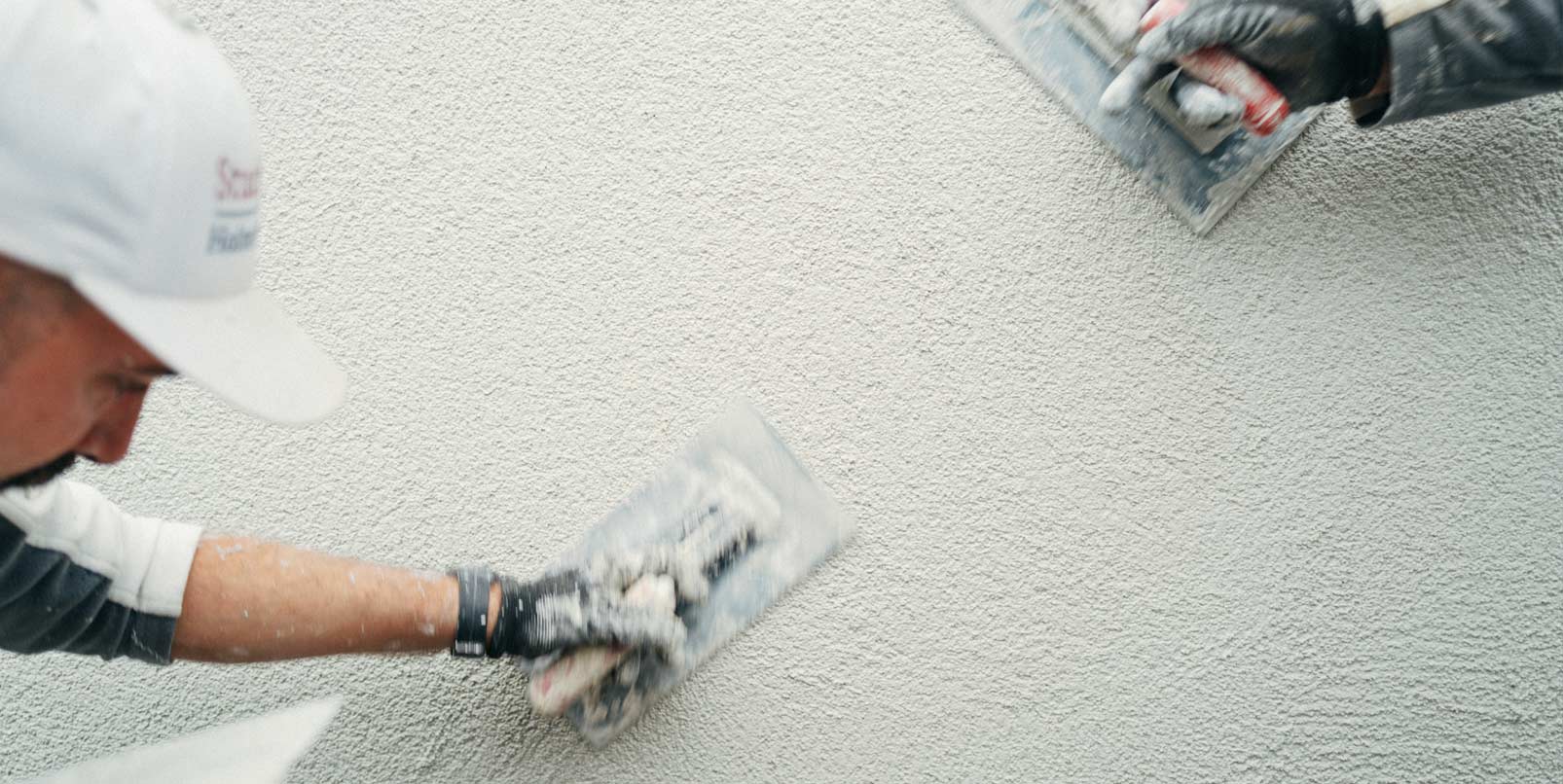 Detailbild von zwei Händen mit Kellen beim Verputzen einer Wand